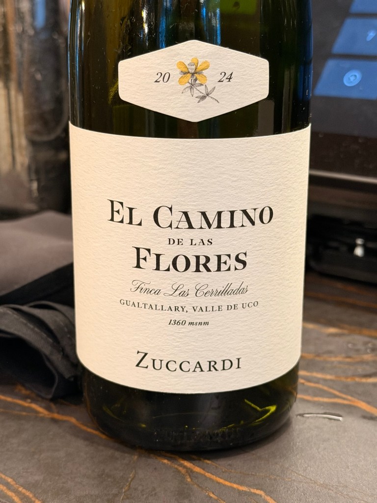 A close-up of a wine bottle labeled 'El Camino de las Flores' by Zuccardi, vintage 2024, showcasing a floral design and details about the vineyard and elevation.