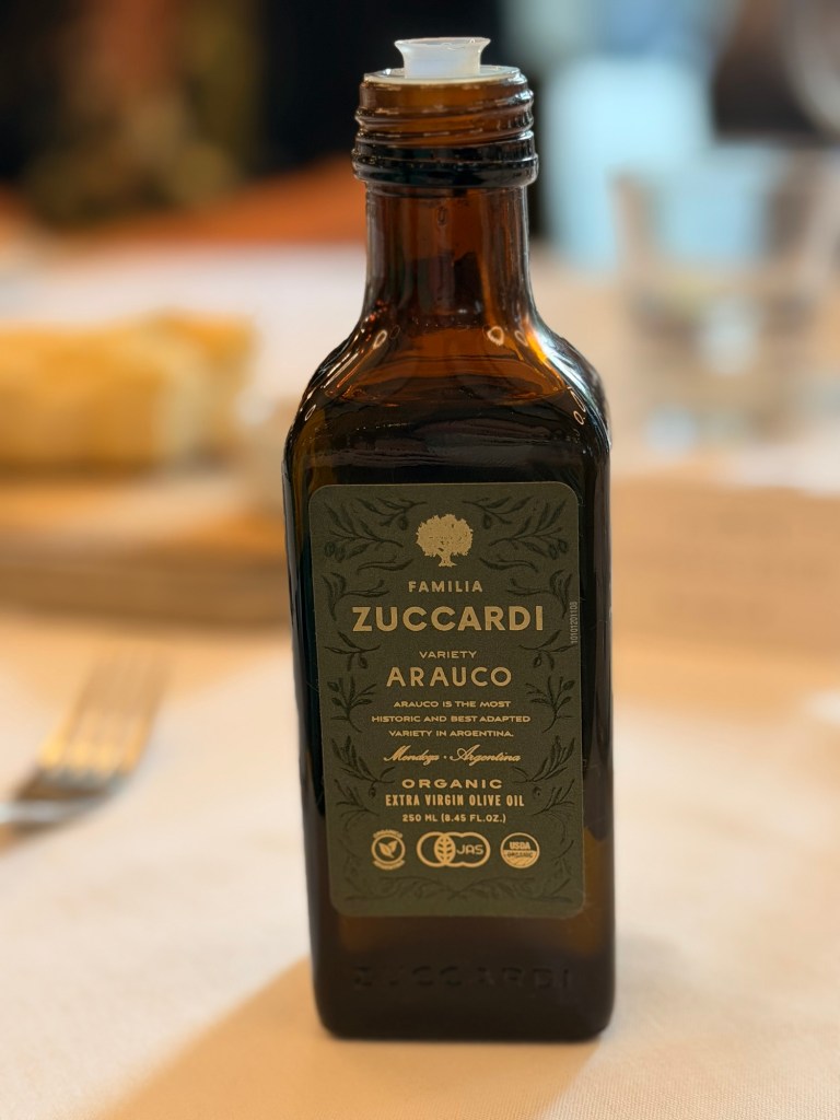 A glass bottle of organic extra virgin olive oil by Familia Zuccardi, labeled as Arauco variety, highlighting its historical significance in Argentina.