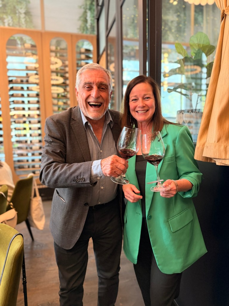 Two smiling people holding wine glasses in a restaurant setting, celebrating with drinks.